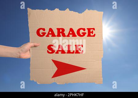 Femme tenant signe avec texte VENTE DE GARAGE contre ciel bleu Banque D'Images