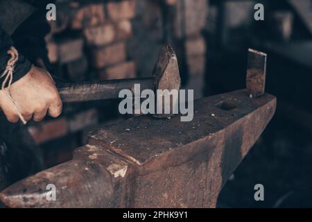 Forgeron en métal avec marteau et pince sur enclume en forge. Le fer à farrier frappe dans l'atelier. Matériel et outils de travail des métaux, de fabrication Banque D'Images