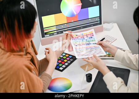 Image rapprochée de deux graphistes féminins qui planifient ensemble un nouveau projet et choisissent la couleur à partir d'un échantillon de nuance de couleur. Banque D'Images