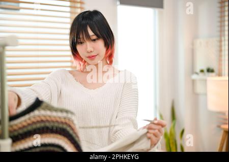 Belle et charmante jeune asiatique femme magasin de vêtements de mode vendeur vérifiant la qualité de ses vêtements, travaillant dans son bureau à domicile. Concept d'entreprise PME Banque D'Images