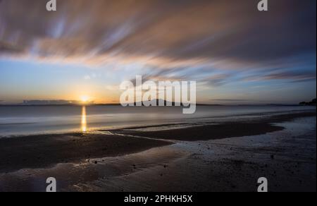 Image d'exposition longue du soleil levant au-dessus de l'île Rangitoto, nuages qui dérivent au-dessus. Milford Beach, Auckland. Banque D'Images