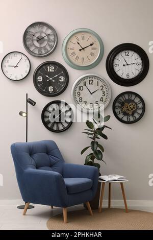 Fauteuil, table et de nombreuses horloges différentes accrochées au mur blanc dans la chambre Banque D'Images