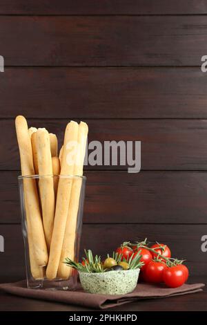 Délicieux graissini frais en verre, olives au romarin et tomates sur table en bois Banque D'Images