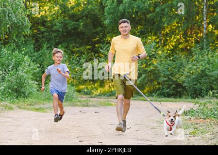 Le père et le fils font du jogging le long de la route de terre de campagne avec un chien sur la laisse de la taille Banque D'Images