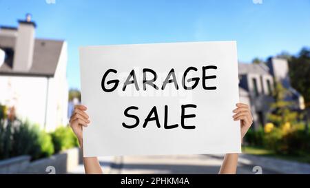 Femme tenant l'affiche avec texte VENTE DE GARAGE sur la rue, gros plan Banque D'Images