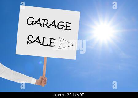 Femme tenant signe avec texte VENTE DE GARAGE contre ciel bleu Banque D'Images