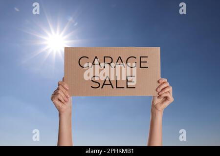 Femme tenant signe avec texte VENTE DE GARAGE contre ciel bleu Banque D'Images