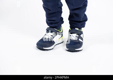 Chaussures pour enfants. Chaussures de course à pied bleues pour enfants sur les jambes d'un garçon de cinq ou six ans sur fond blanc. Banque D'Images