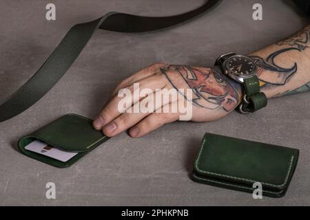 Main d'un homme avec une montre sur son poignet. Articles d'artisanat en cuir, ceinture, porte-carte de crédit, bracelet de montre. Style pour Homme Banque D'Images