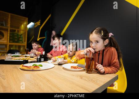 Quatre enfants mangent de la pizza italienne dans la pizzeria. Les enfants mangent au café. Jus de boisson pour fille. Banque D'Images