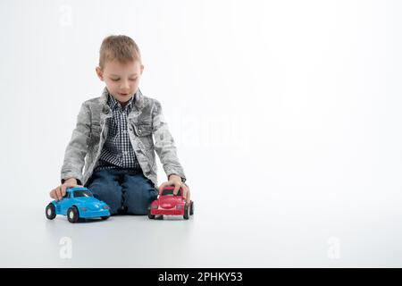 Un jeune garçon joue avec des voitures-jouets multicolores sur fond blanc.Divertissement pour les enfants, divertissement. Banque D'Images