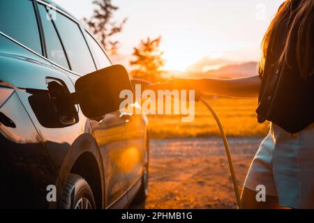 Jeune femme brancher le chargeur dans une voiture électrique noire, concept d'énergie renouvelable Banque D'Images