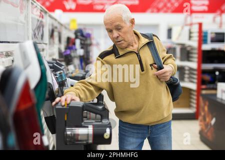 Sénior homme retraité achetant l'aspirateur vertical dans la salle d'exposition du magasin d'appareils électriques Banque D'Images