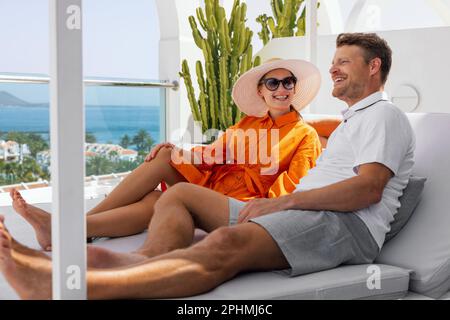 couple souriant se détendre dans un transat et profiter des vacances d'été à la terrasse de villa de luxe Banque D'Images