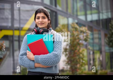 Une étudiante d'université ou d'université à l'extérieur d'un bâtiment de campus portant un casque sans fil Banque D'Images