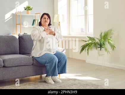 Jeune femme de poids lourd assise sur le canapé souffrant de problèmes cardiaques. Banque D'Images