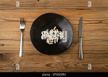 Capsules de médicaments sur plaque, supplément alimentaire, vitamines de plantes, surdosage, médicaments concept d'excès, Beaucoup de pilules Brown sur Black plate Top View Banque D'Images