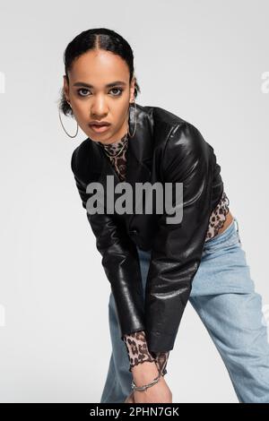 femme afro-américaine tendance en veste courte tendance et jeans bleus regardant l'appareil photo isolé sur gris, image de stock Banque D'Images