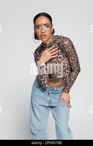 modèle afro-américain élégant avec imprimé animal et lunettes de soleil tendance posé isolé sur gris, image de stock Banque D'Images