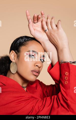 portrait d'une femme afro-américaine élégante dans un blazer rouge vif en train de regarder l'appareil photo isolé sur beige, image de stock Banque D'Images