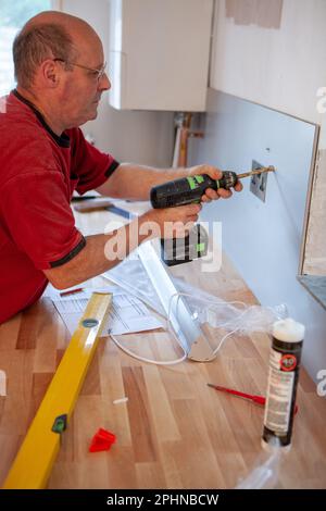 Appareils de cuisine : montage de la splashback. Un monteur prenant soin de monter une nouvelle pièce de cuisine en métal en position. À partir d'une série d'images associées. Banque D'Images