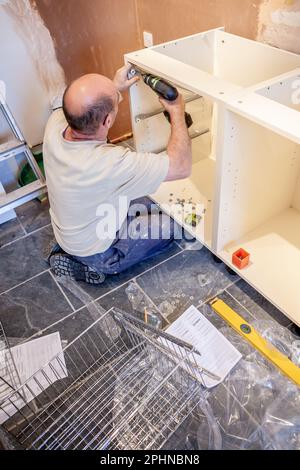 Cuiseurs de cuisine : installation des tiroirs. Un monteur qui travaille à l'installation des tiroirs sur la carcasse d'une nouvelle cuisine. À partir d'une série d'images associées. Banque D'Images