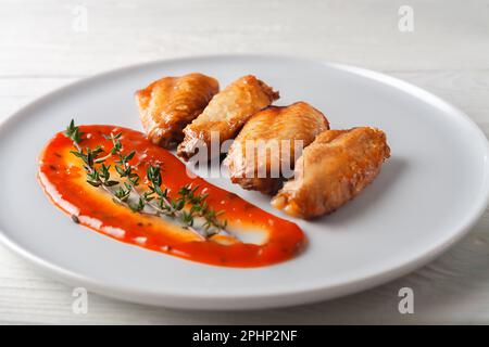 Ailes de poulet épicées grillées avec ketchup sur une assiette sur fond blanc. Banque D'Images