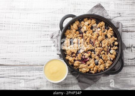 Tarte aux fruits aux baies d'été Smulpaj, cuite avec des pommes et des bleuets, servie avec de la sauce à la vanille dans une casserole sur la table. Vue horizontale du dessus de l'ab Banque D'Images