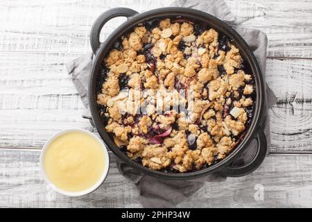 Crumble aux fruits rouges cuit avec des pommes et des bleuets servis avec une sauce à la vanille dans une casserole sur la table. Vue horizontale du dessus Banque D'Images