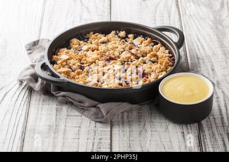 Tarte aux fruits aux baies d'été Smulpaj, cuite avec des pommes et des bleuets, servie avec de la sauce à la vanille dans une casserole sur la table. Horizontale Banque D'Images