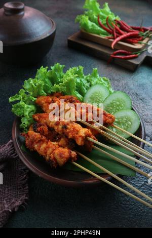 poulet épicé rouge satay avec des tranches de ​​cucumber et de la laitue sur une assiette en argile avec des piments rouges en arrière-plan Banque D'Images