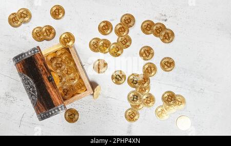 Petit coffre décoré en bois avec des pièces en or de la BTC ( bitcoin crypto-monnaie ), plus éparpillées sur le panneau de pierre blanche, photo d'en haut Banque D'Images