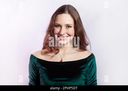 Portrait d'une femme souriante heureuse et attrayante portant une robe verte debout regardant l'appareil photo avec un sourire crasseux, exprimant des émotions positives aimables. Prise de vue en studio isolée sur fond gris. Banque D'Images