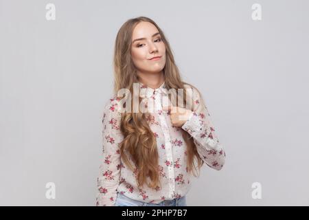 C'est moi. Portrait d'une femme arrogante avec des cheveux blonds ondulés pointant vers elle-même, regardant égoïste et haughty, fier de l'accomplissement. Prise de vue en studio isolée sur fond gris. Banque D'Images