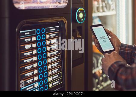 Le client paie le produit au distributeur automatique en utilisant le mode de paiement sans contact avec le téléphone portable. Homme utilisant l'application de paiement sur smartphone pour acheter produ Banque D'Images