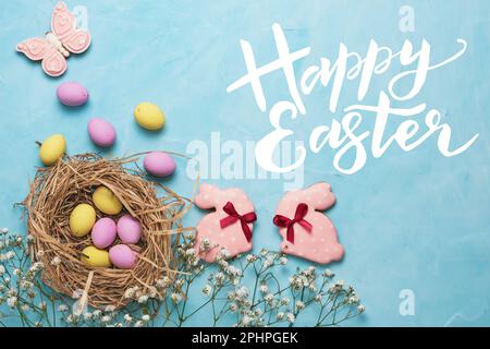 Bannière pour les vacances de Pâques. Oeufs colorés dans un nid de paille et fleurs blanches de printemps sur fond bleu. Placer pour le texte. Vue de dessus. Banque D'Images