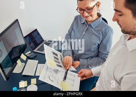 Femme entrepreneur discutant des données financières avec sa collègue debout à son bureau. Bonne femme d'affaires positive travaillant avec des tableaux et une table Banque D'Images