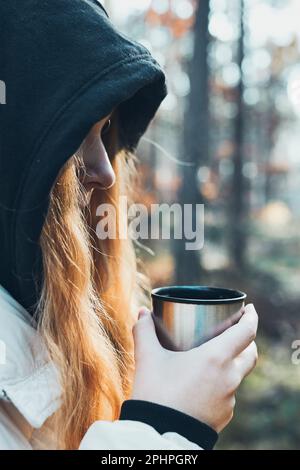 Femme dans une hotte ayant une pause pendant le voyage d'automne tenant une tasse avec une boisson chaude de thermos fiole le jour d'automne froid. Fille active errant dans une forêt ac Banque D'Images