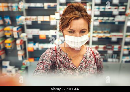 Une femme qui fait ses courses à la pharmacie, achète des médicaments, porte un masque facial pour couvrir la bouche et le nez pendant l'éclosion du coronavirus pandémique Banque D'Images