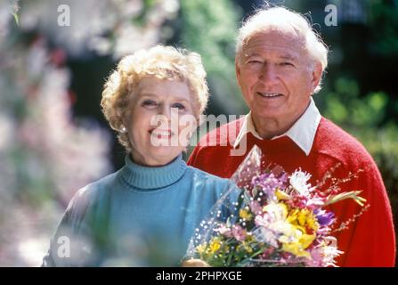 1991 VISAGES HISTORIQUES SOURIANTS DE COUPLE SENIOR DEBOUT ENSEMBLE PRINTEMPS CERISIERS EN FLEURS DANS PARK Banque D'Images