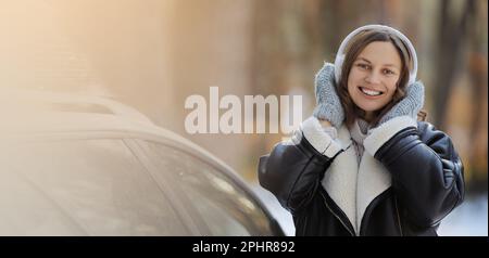 Happy Woman est en train d'écouter de la musique dans des écouteurs, de danser tout en emballant l'arbre de Noël avec le filet et les guirlandes sur un toit de sa voiture, se préparer à un Banque D'Images