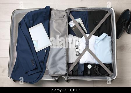 Vêtements pliés avec accessoires dans une valise ouverte et chaussures sur parquet, plat. Planification de voyages d'affaires Banque D'Images