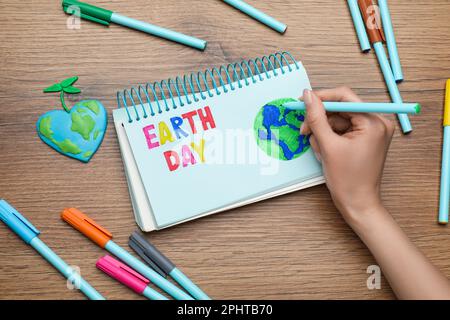Bonne journée de la Terre. Femme dessin planète dans un carnet à table en bois, vue de dessus Banque D'Images