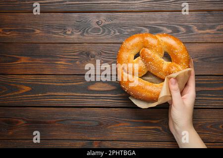 Femme avec de savoureux bretzel fraîchement cuit à table en bois, vue de dessus. Espace pour le texte Banque D'Images