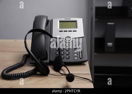 Téléphone fixe et casque sur un bureau en bois à l'intérieur. Service d'assistance téléphonique Banque D'Images