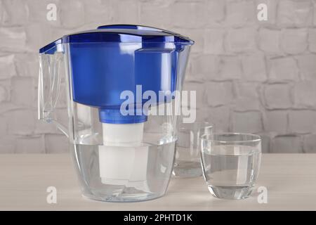 Verseuse filtrante et verre avec eau purifiée sur table blanche à l'intérieur Banque D'Images