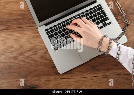 Femme avec clavier en chaîne sur ordinateur portable à table en bois, vue de dessus. Dépendance à l'Internet Banque D'Images