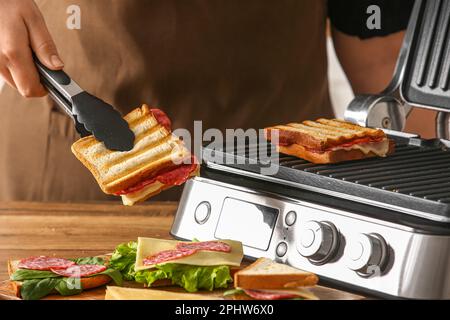 Femme tenant un délicieux sandwich avec des pinces près du gril électrique moderne Banque D'Images