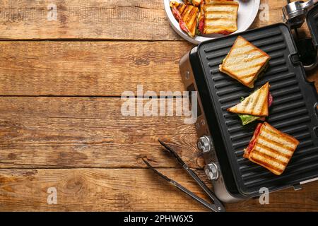 Gril électrique moderne avec délicieux sandwiches sur une table en bois Banque D'Images