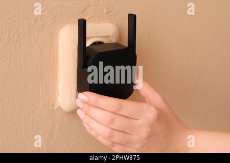 Femme qui branche le répéteur WiFi noir dans la prise électrique murale beige Banque D'Images